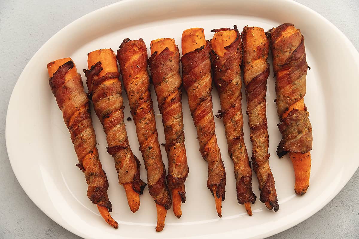 cooked bacon wrapped carrots on a white platter