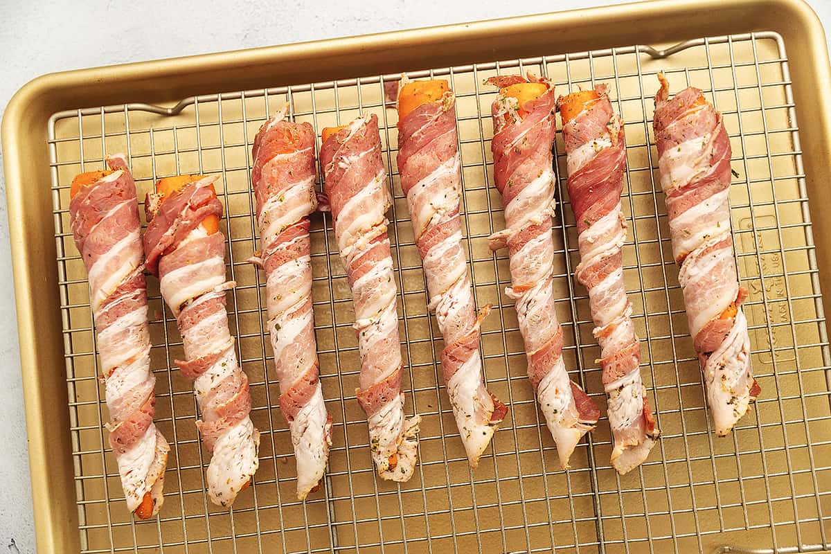 bacon wrapped around carrots on a sheet pan with a wire rack