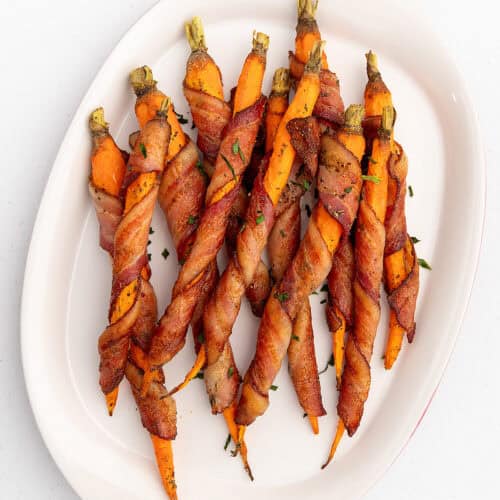 bacon wrapped carrots on a white serving platter