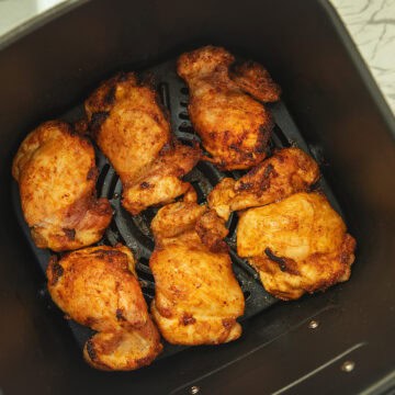 an air fryer basket containing cooked boneless skinless chicken thighs