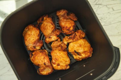 an air fryer basket containing cooked boneless skinless chicken thighs