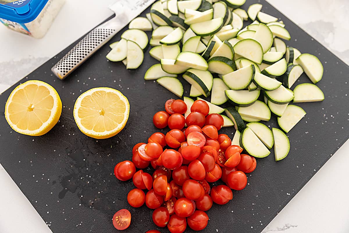 Sliced zucchini and tomatoes on a black cutting board