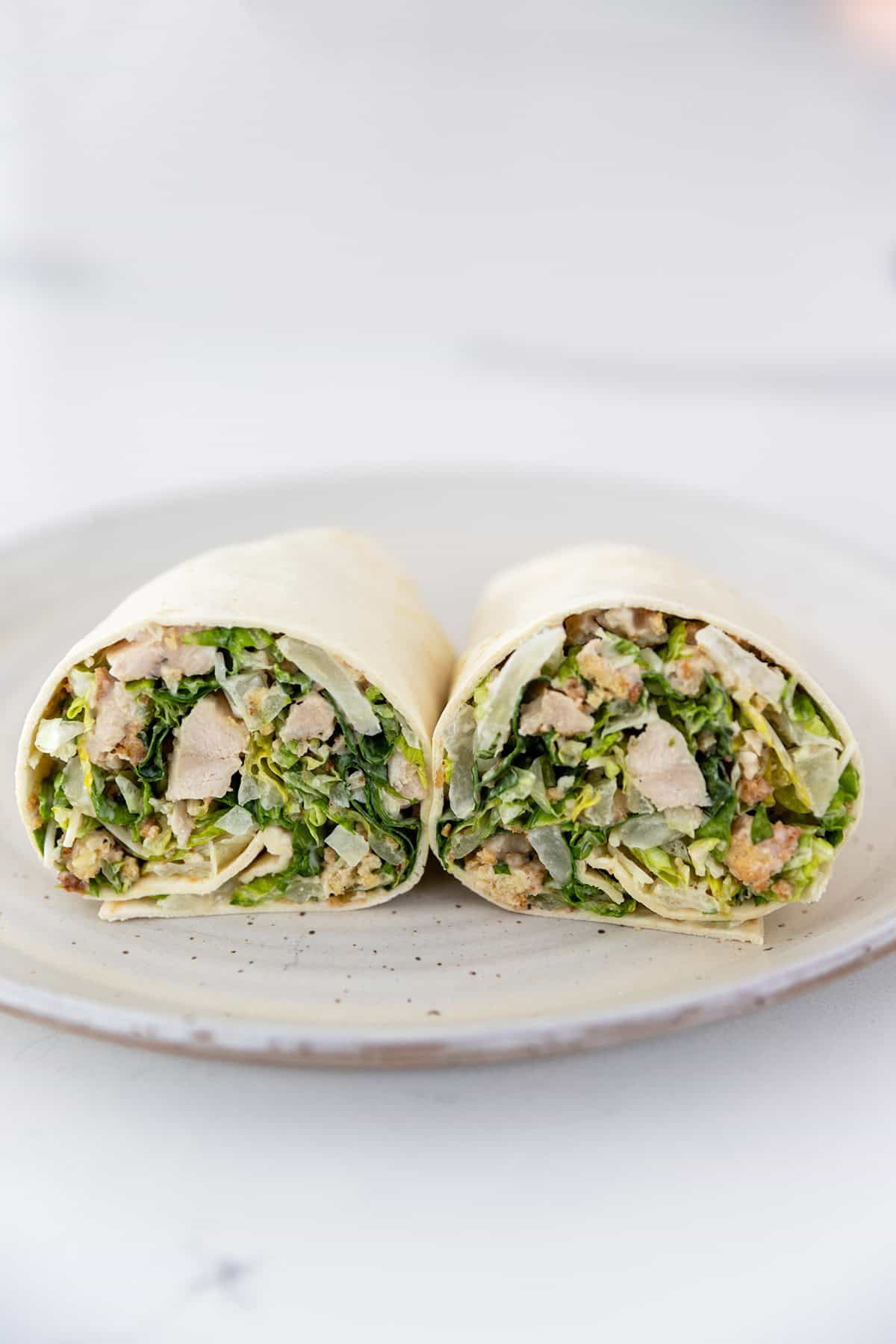 chicken caesar wrap cut in half on a white plate