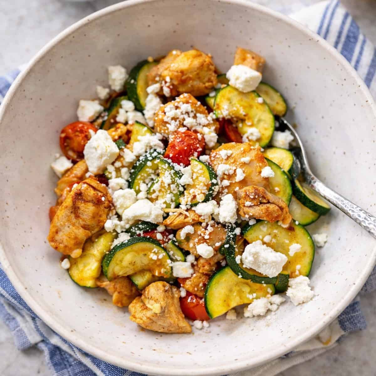 Finished meal in a bowl of chicken and zucchini with tomatoes and feta