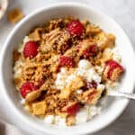 Healthy cottage cheese breakfast bowl with raspberries, crunchy cereal, almond butter, hemp hearts, and cinnamon in a white bowl.