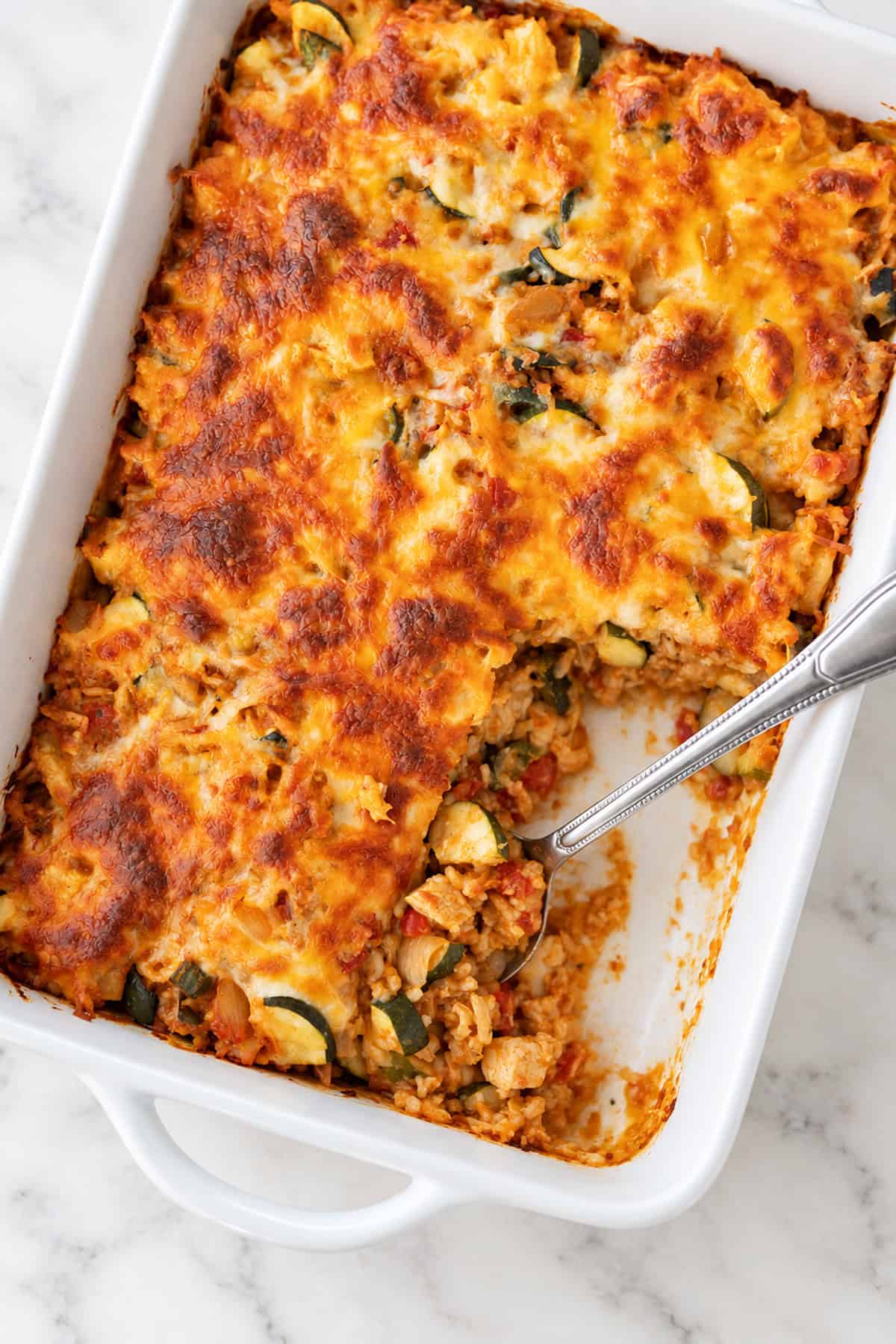 High protein chicken taco casserole with golden melted cheese in a white baking dish.