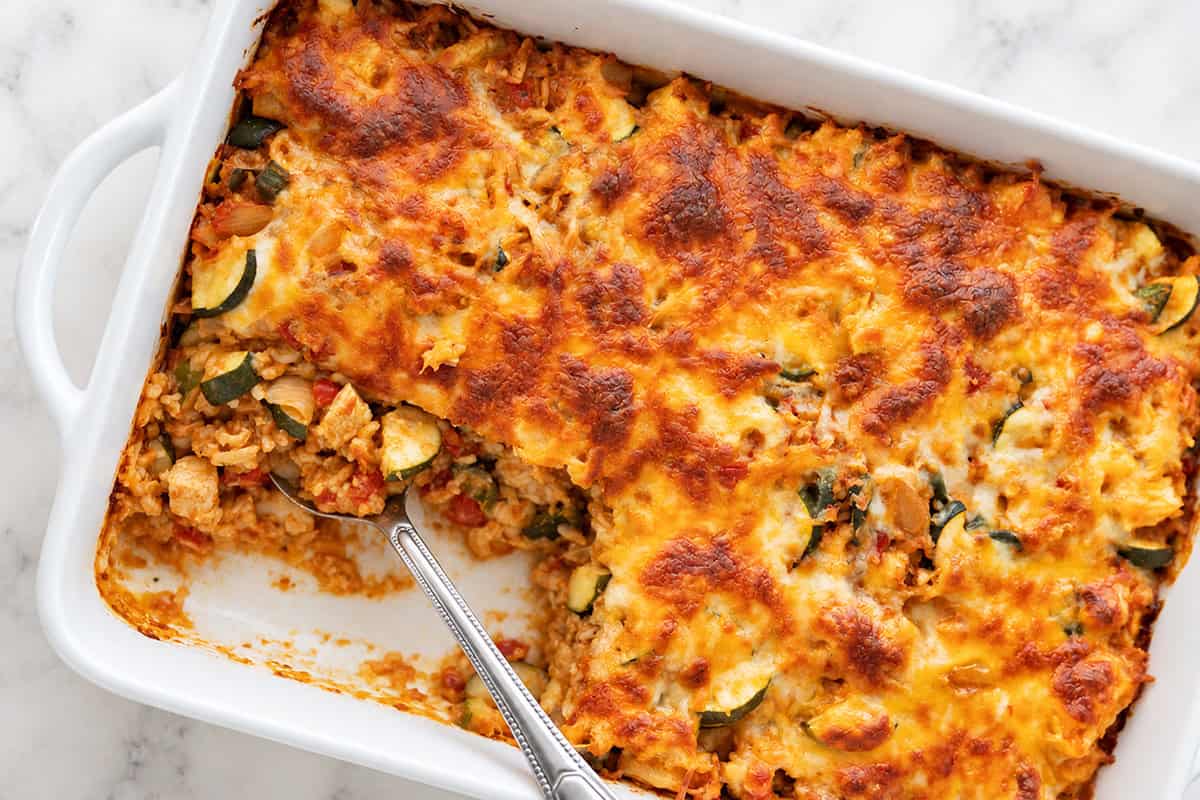 Chicken taco casserole with a portion scooped out, showing chicken, rice, and vegetables.